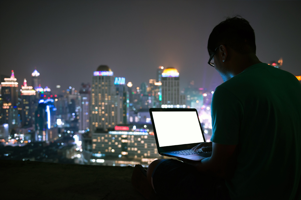 person using laptop, skyline with city lights in background, night